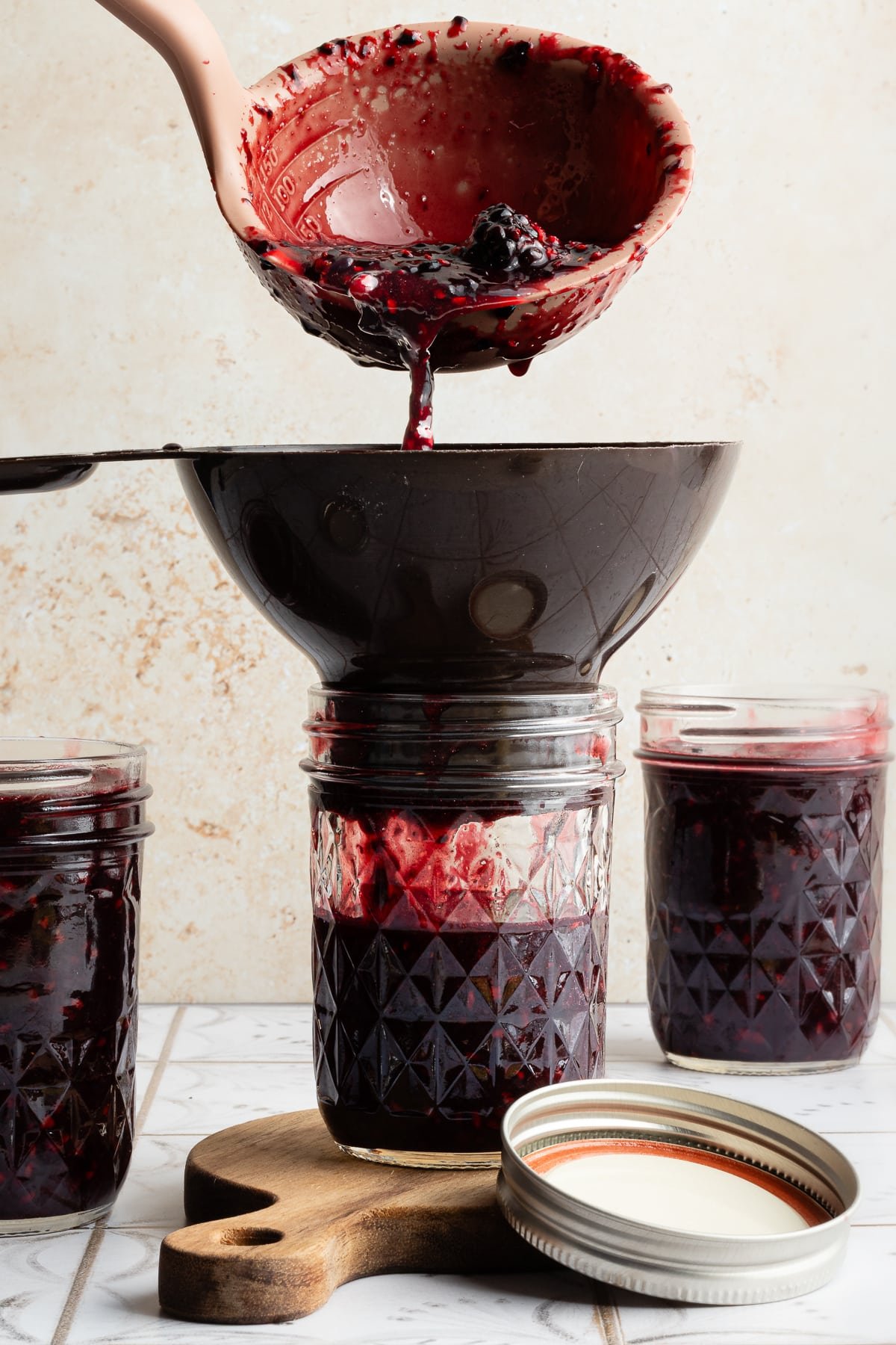 Blackberry jam being poured into glass mason jars. 