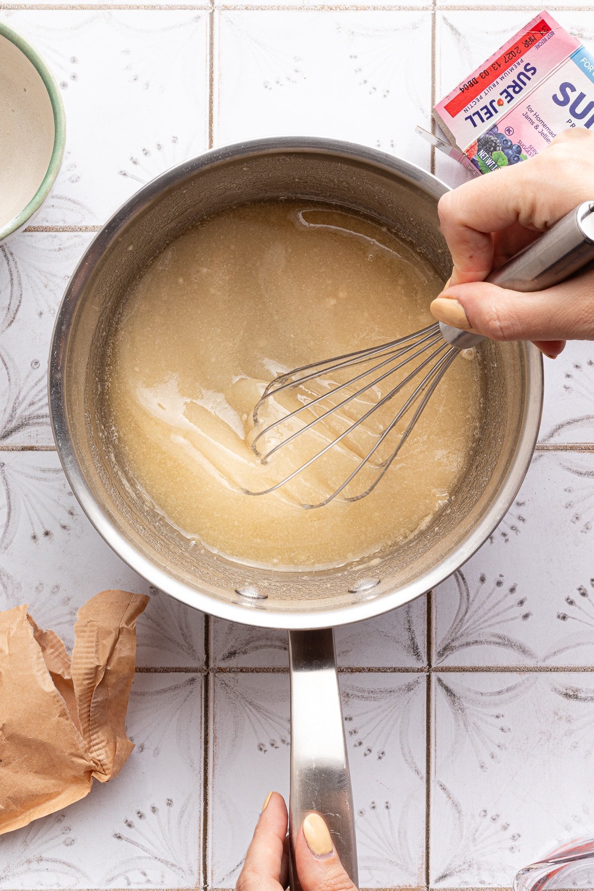 Pectin and sugar being mixed with water in a saucepan.