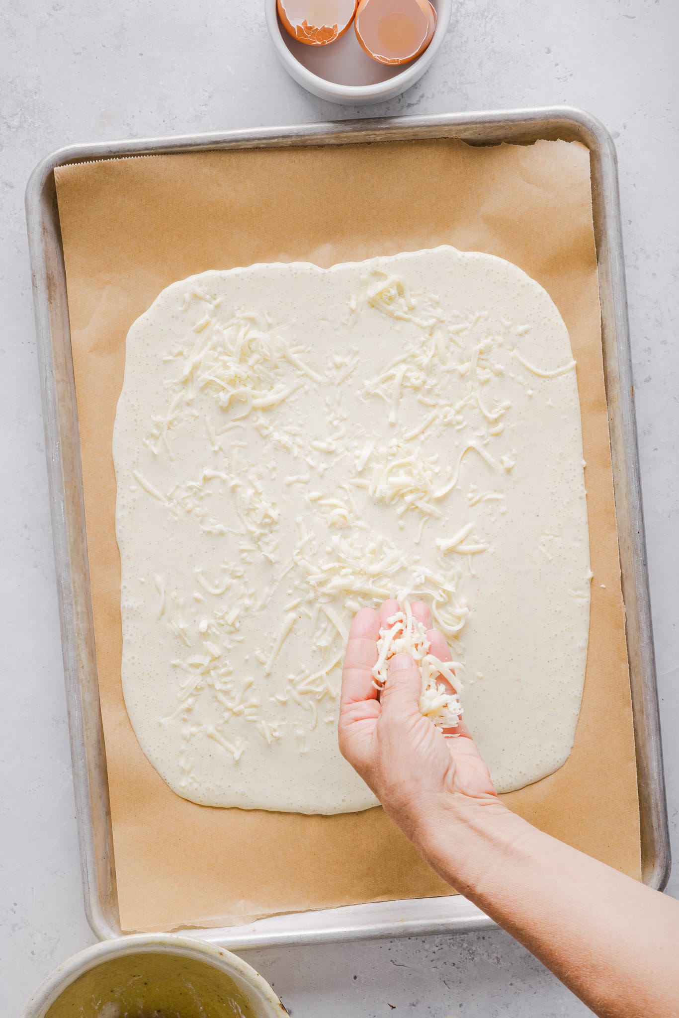 Blended egg and cottage cheese mixture spread onto a sheet pan with mozzarella being sprinkled on top.