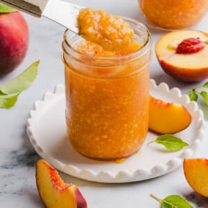 Peach freezer jam in a glass jar with a knife taking out a scoop.