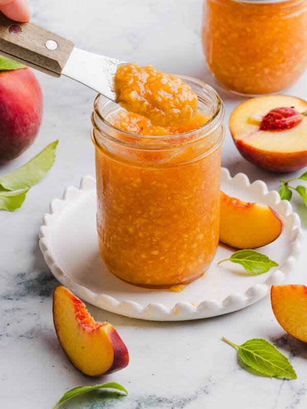 Peach freezer jam in a glass jar with a knife taking out a scoop.