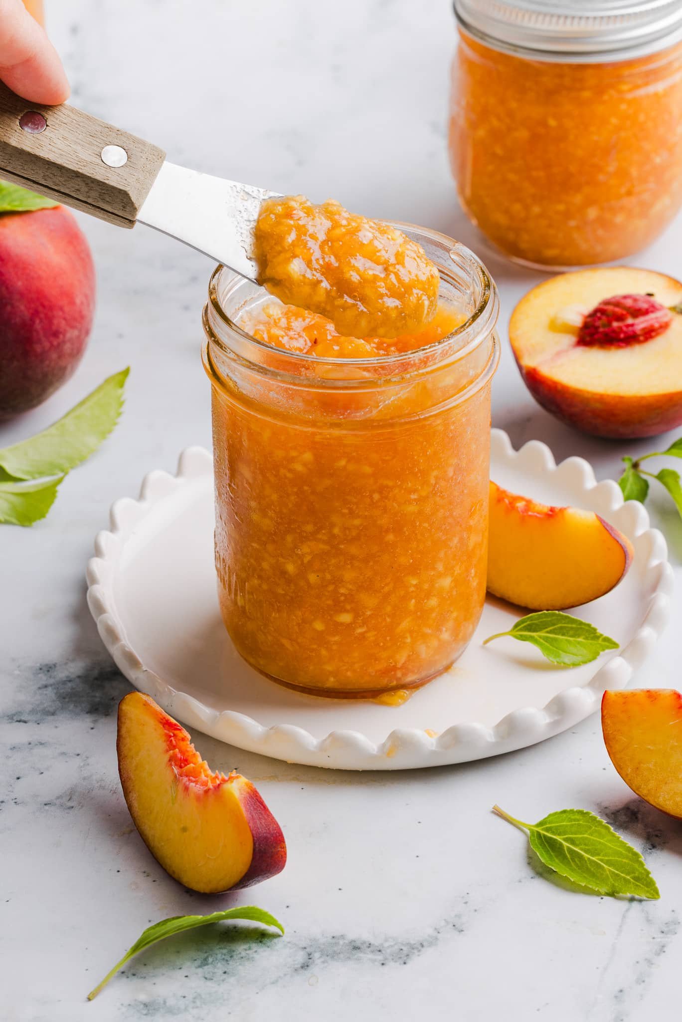 Peach freezer jam in a glass jar with a knife taking out a scoop.