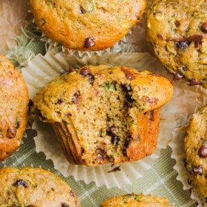 Protein zucchini muffins on a countertop with a bite taken out of one.