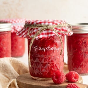 Raspberry freezer jam in a jar with a checkered cloth and lid.