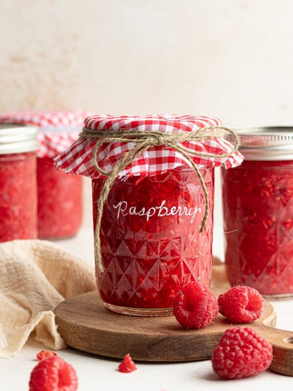 Raspberry freezer jam in a jar with a checkered cloth and lid.