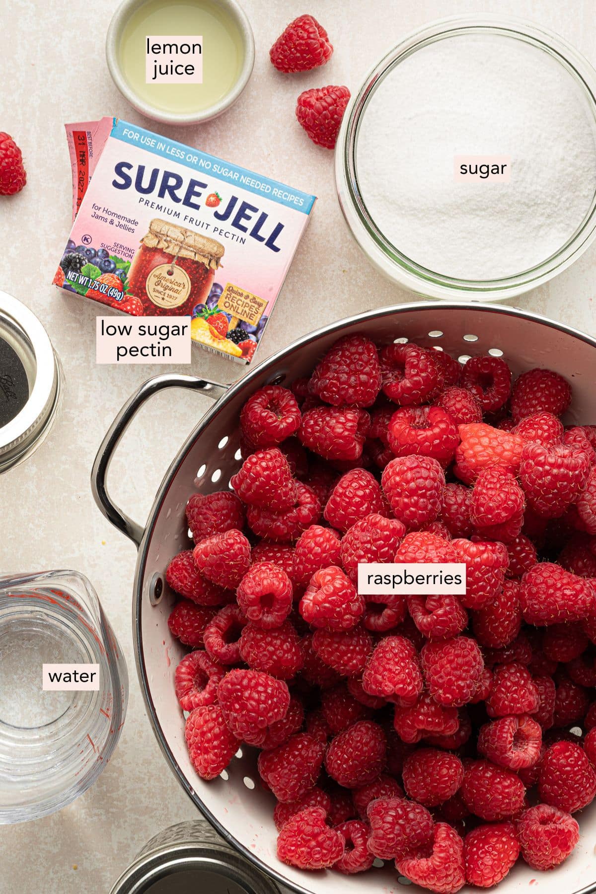 Ingredients for low sugar raspberry freezer jam on a countertop with labels.