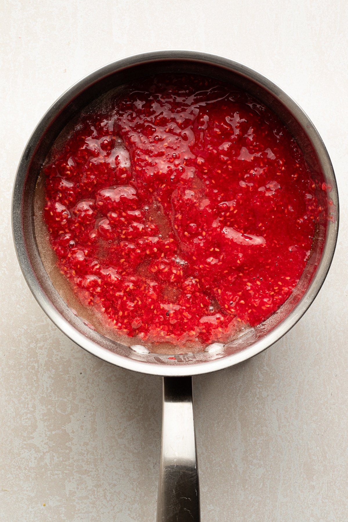 Sugar and pectin being mixed with raspberries in a pan.