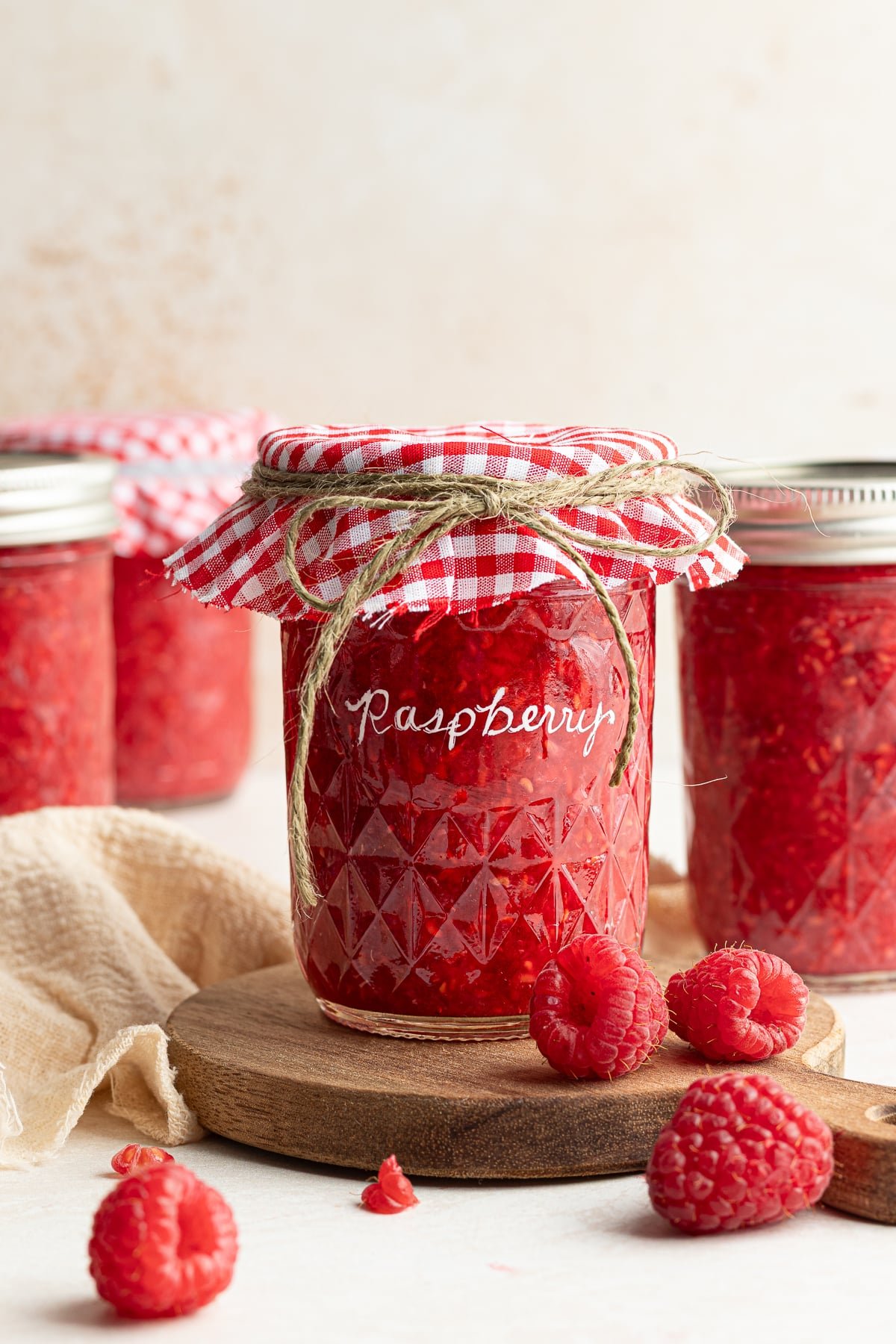 Raspberry freezer jam in a jar with a checkered cloth and lid. 