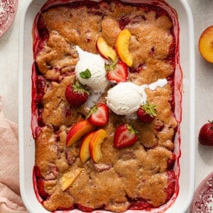 Strawberry peach cobbler topped with fresh peaches, strawberries and vanilla ice cream.