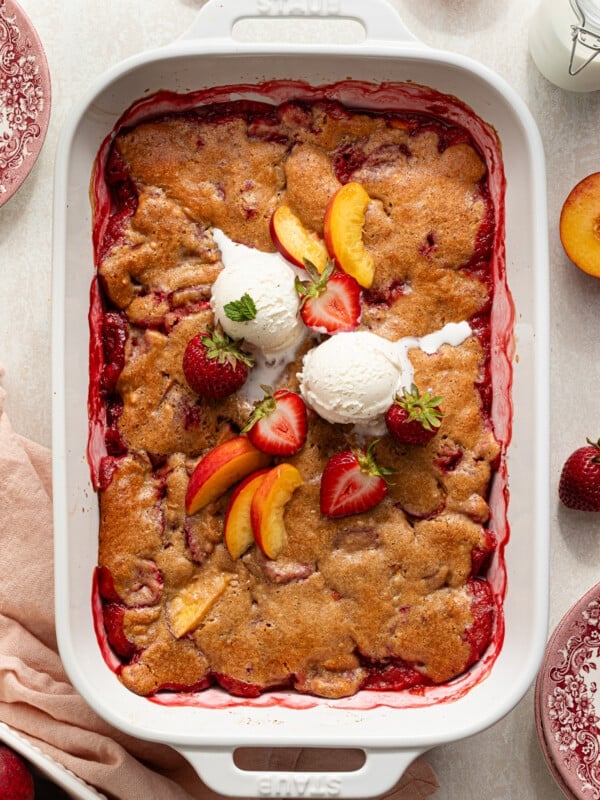 Strawberry peach cobbler topped with fresh peaches, strawberries and vanilla ice cream.