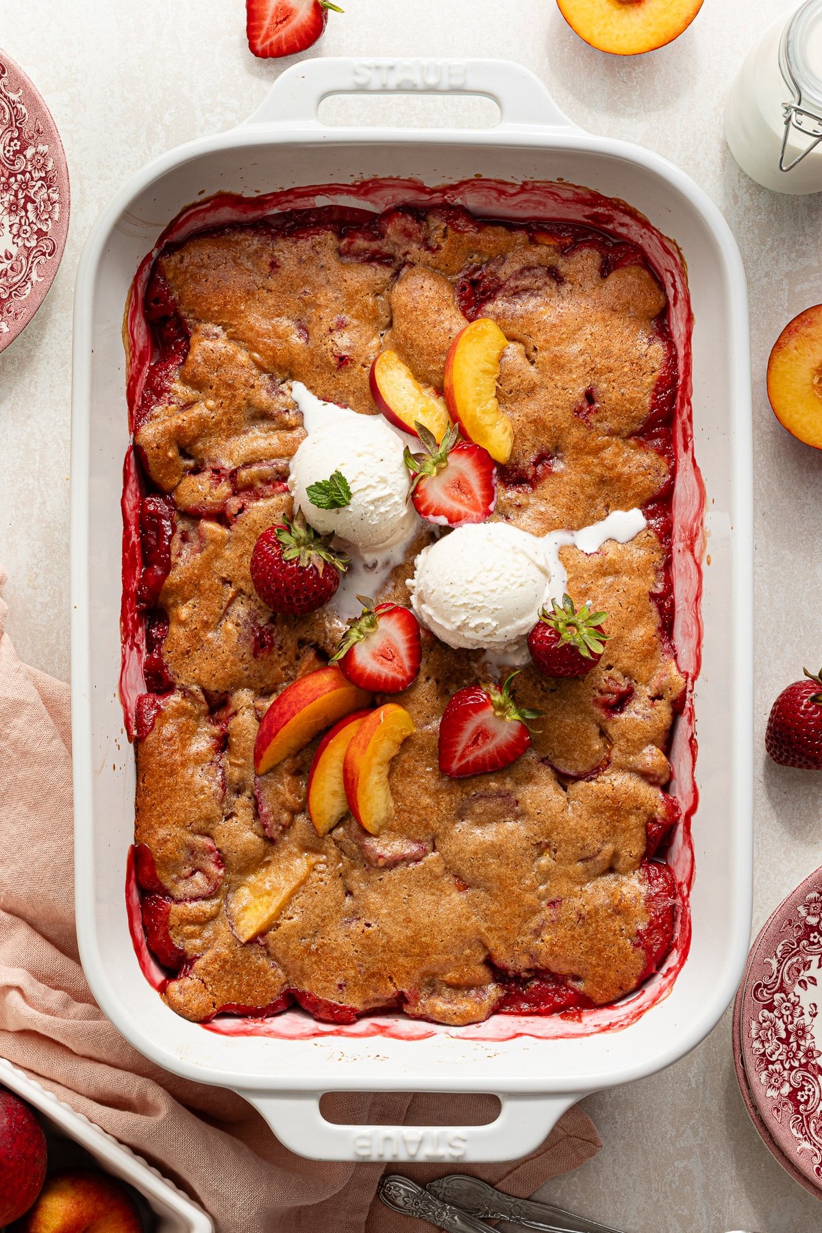 Strawberry peach cobbler topped with fresh peaches, strawberries and vanilla ice cream.