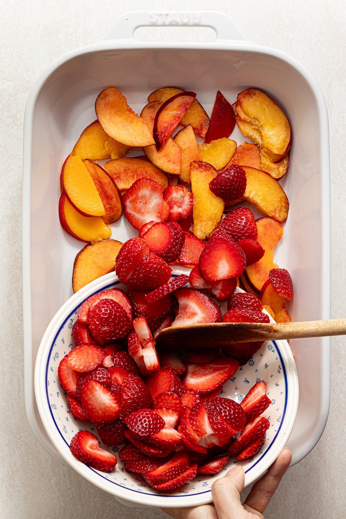 Strawberries and peaches being poured into a baking dish.