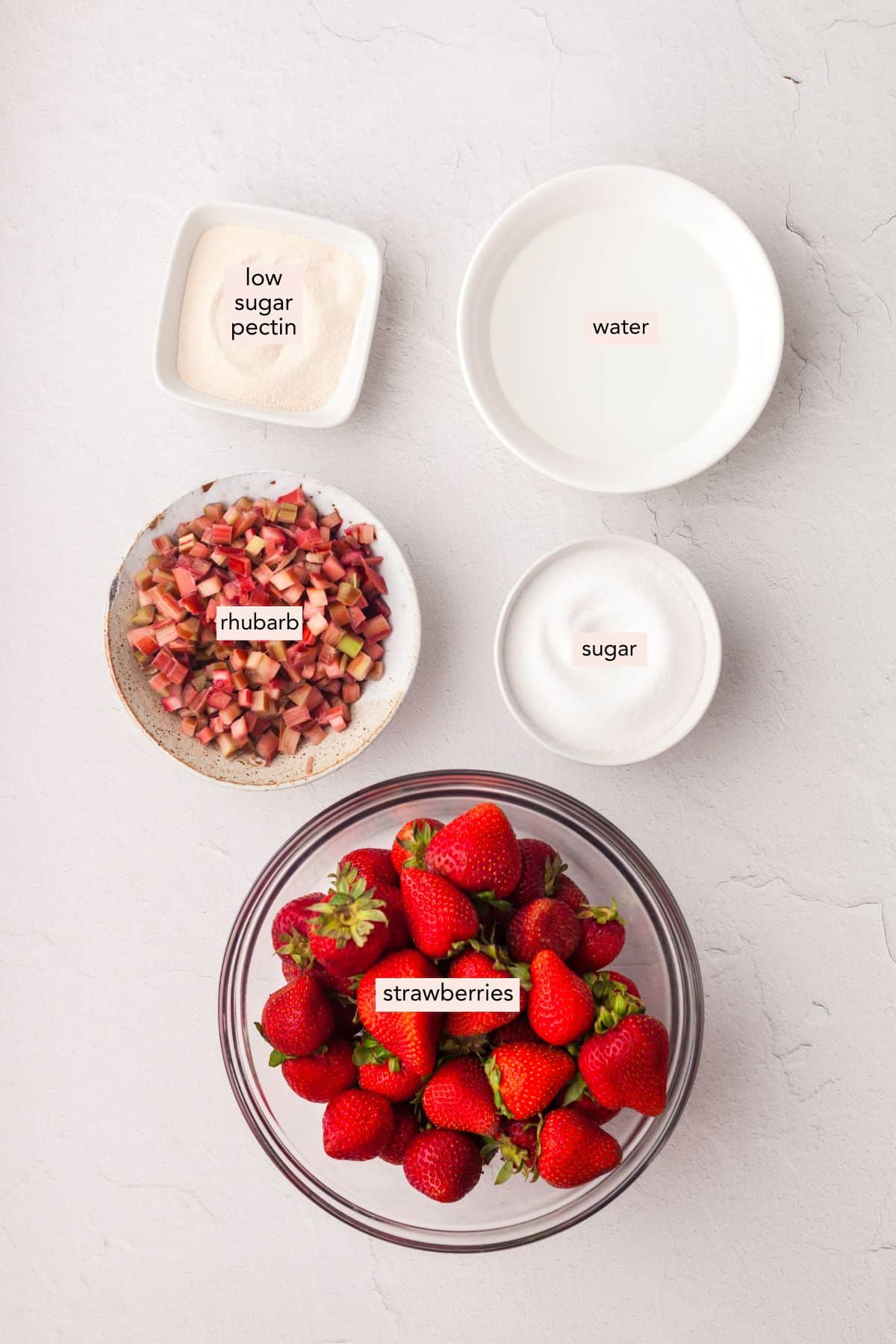 Ingredients for strawberry rhubarb freezer jam on a countertop with labels.