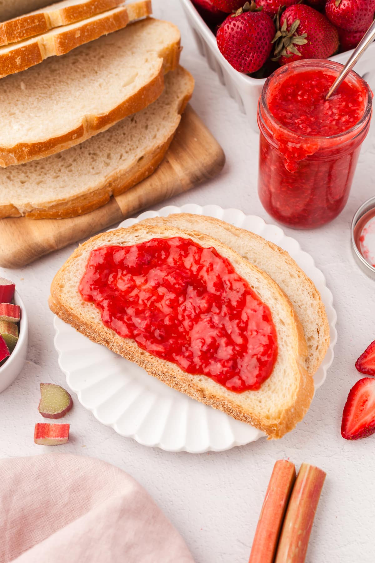 Strawberry rhubarb freezer jam spread on toast on a white scalloped plate.