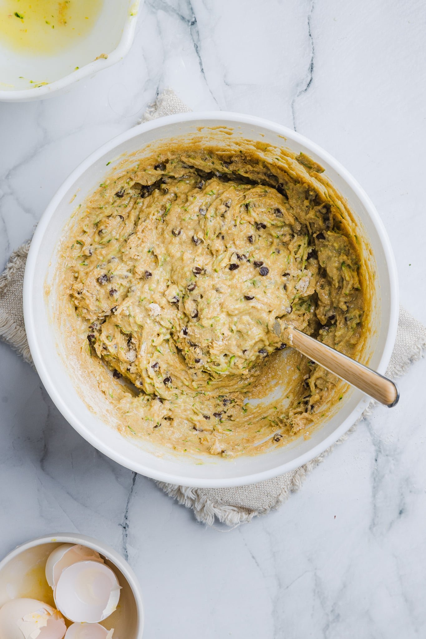 Zucchini protein muffin batter with chocolate chips in a white bowl.