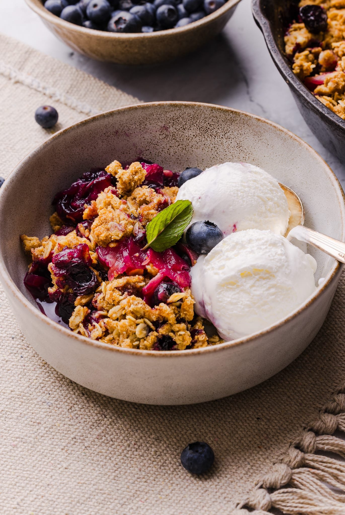 A serving of apple blueberry crumble in a bowl with two scoops of vanilla ice cream.