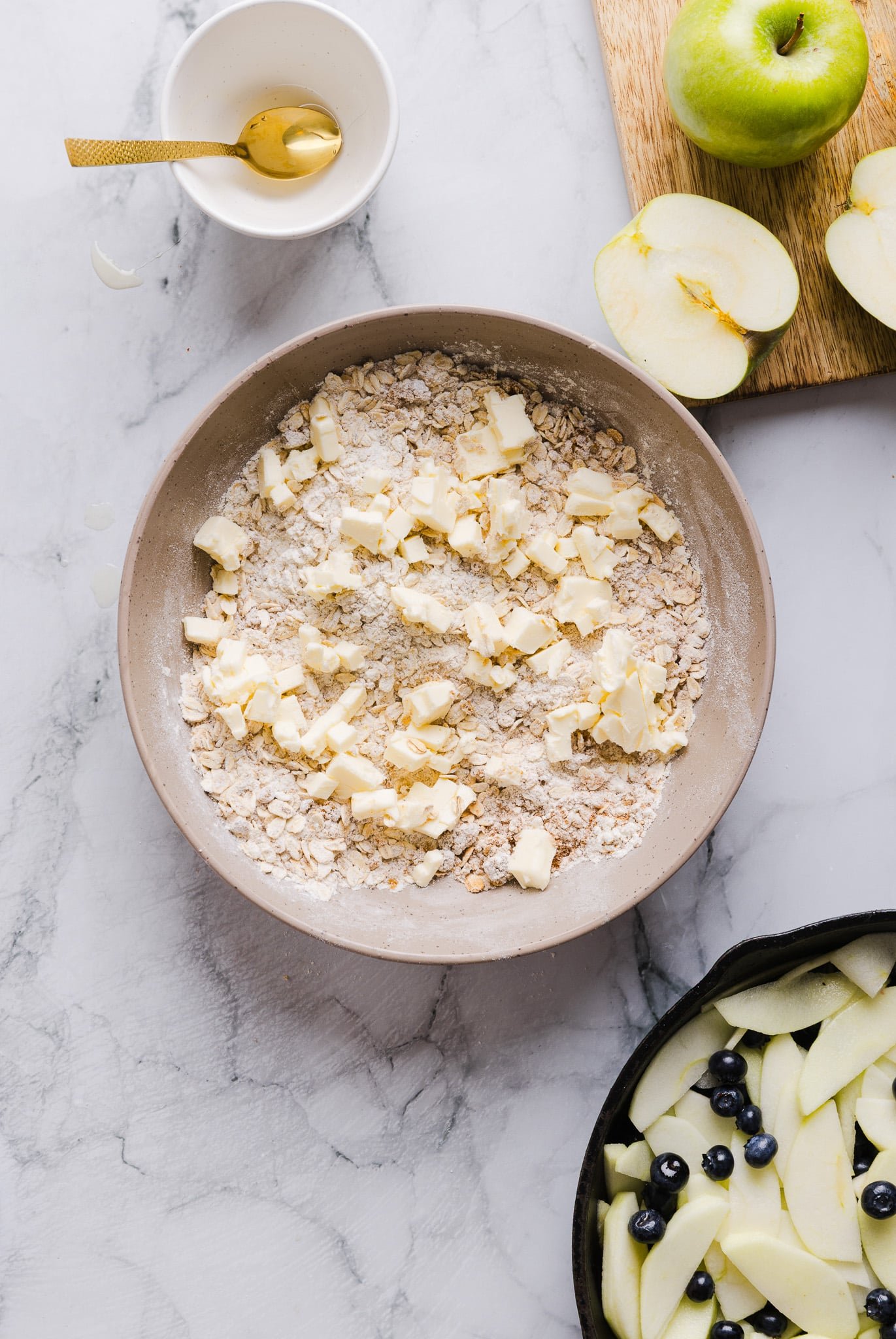 Adding diced butter to a mixture of flour, oats, brown sugar, salt, and cinnamon.