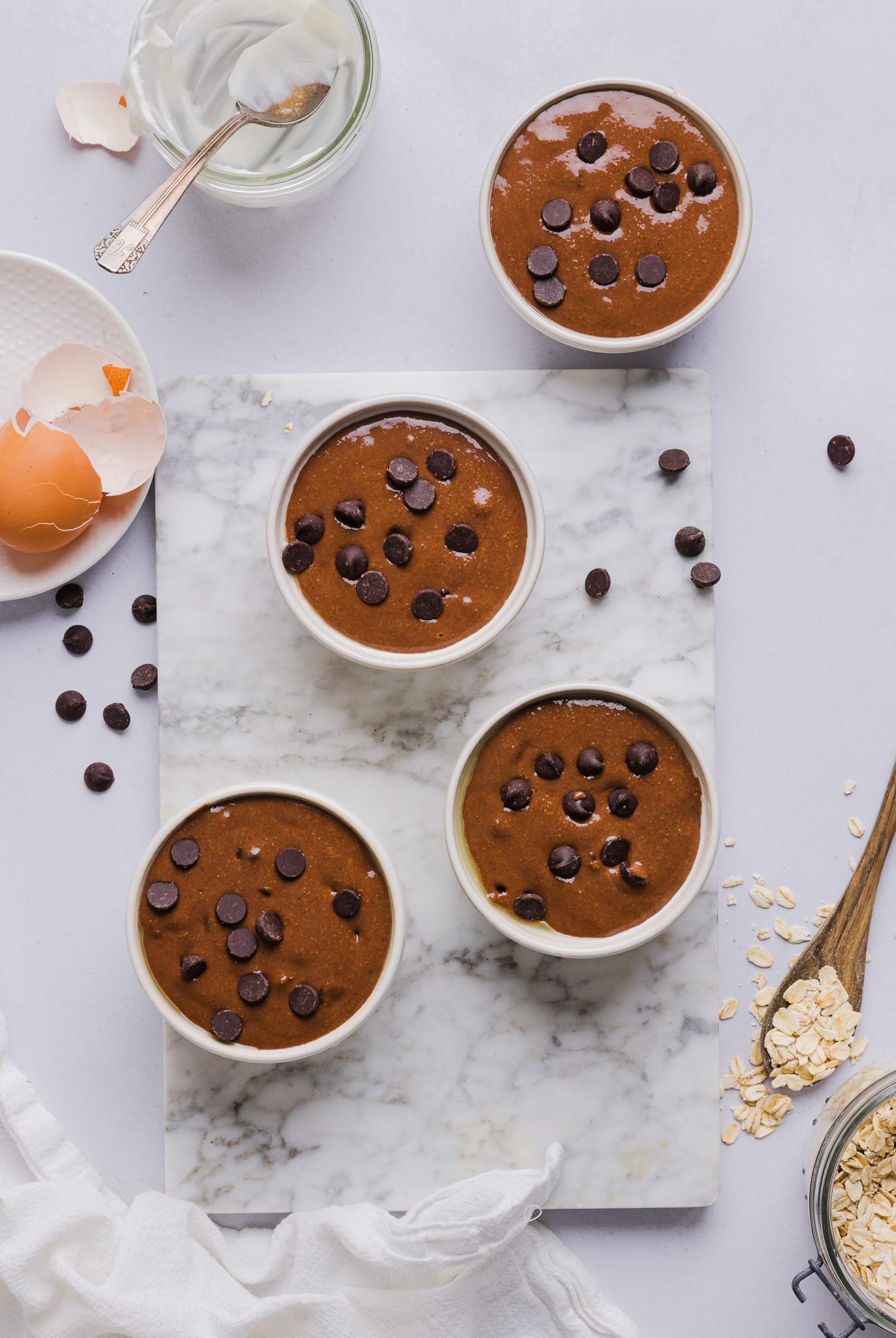 Chocolate baked oats batter poured into ramekins and topped with chocolate chips.