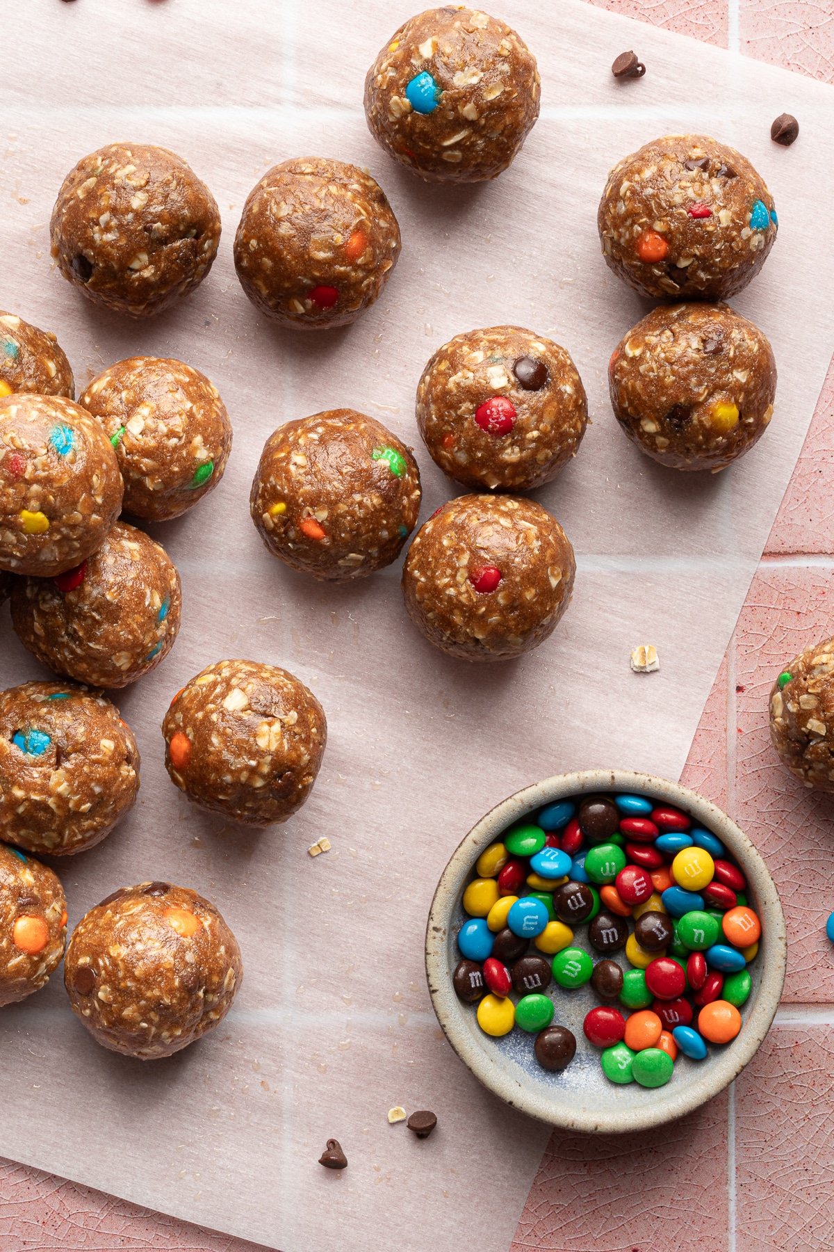 Monster protein balls scattered on a sheet of parchment paper and a small bowl of mini M&Ms.