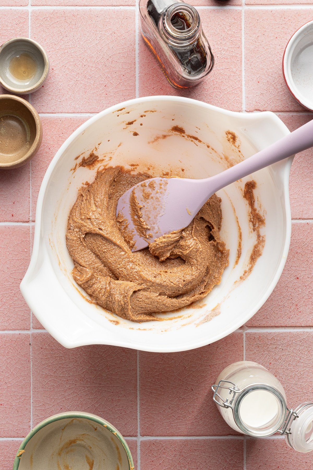 Protein powder, flaxseed, milk and peanut butter in a bowl with maple syrup being poured in.