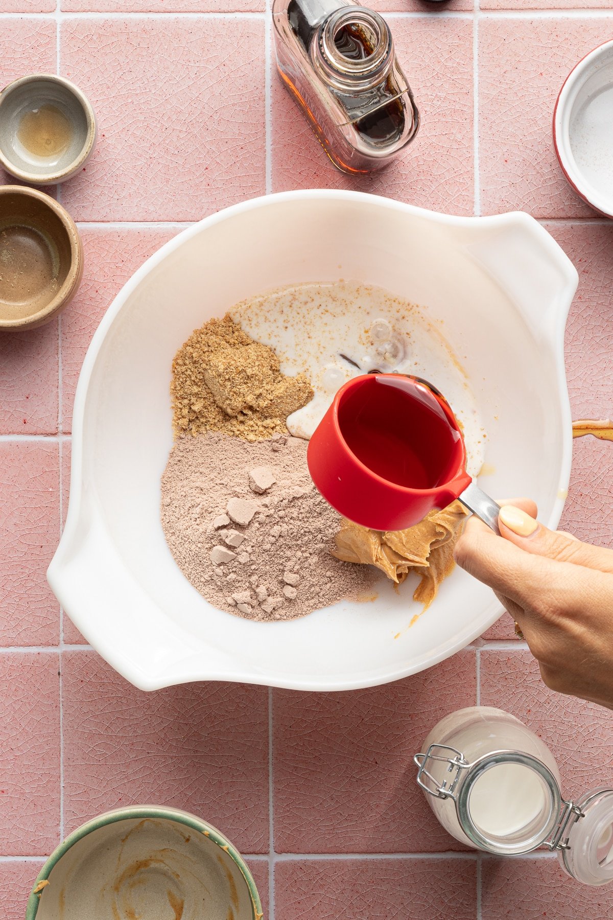 Protein powder, flaxseed, milk and peanut butter in a bowl with maple syrup being poured in.