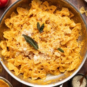 Pasta tossed in protein pumpkin pasta sauce in a pan and garnished with sage.