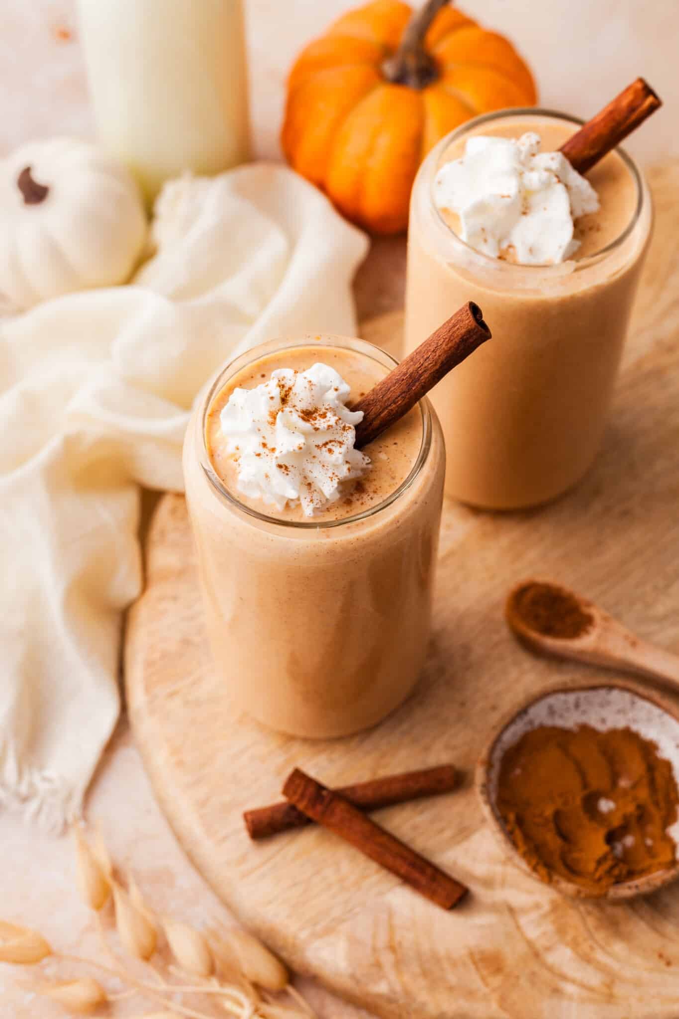 Two pumpkin protein smoothies in glasses and topped with whipped cream.