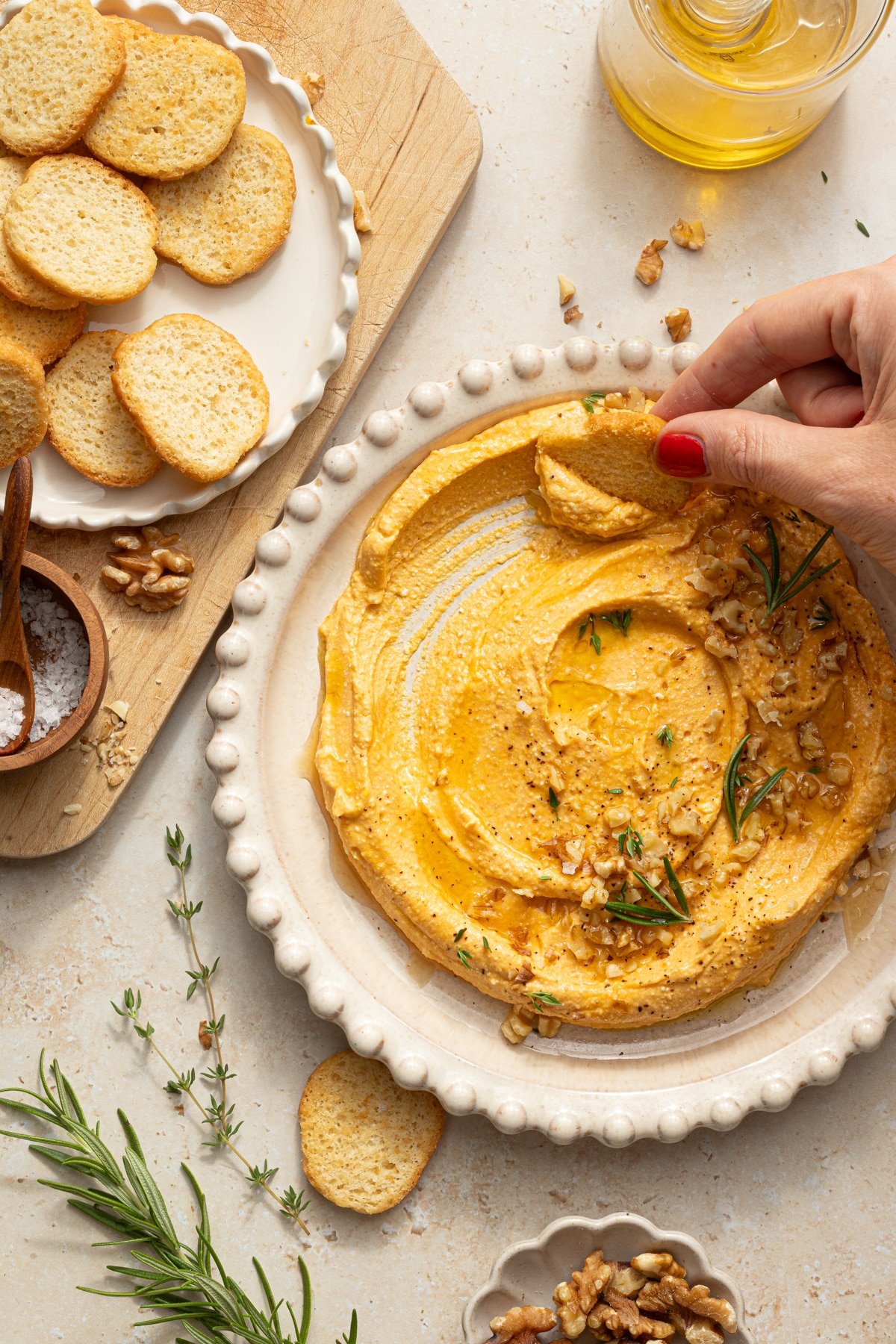 Pumpkin feta dip served next to a dish of crostini, one being by a hand.