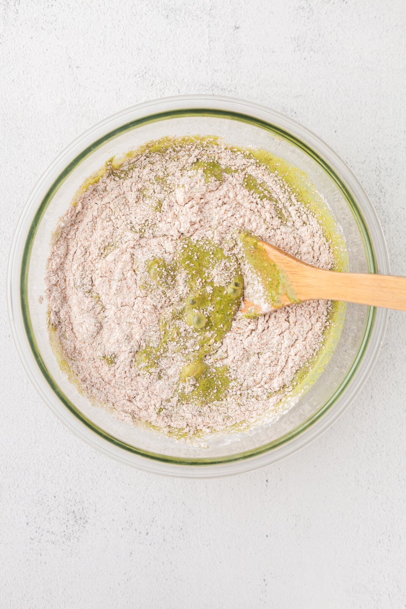 Wet and dry ingredients for spinach banana muffins being mixed in a bowl.