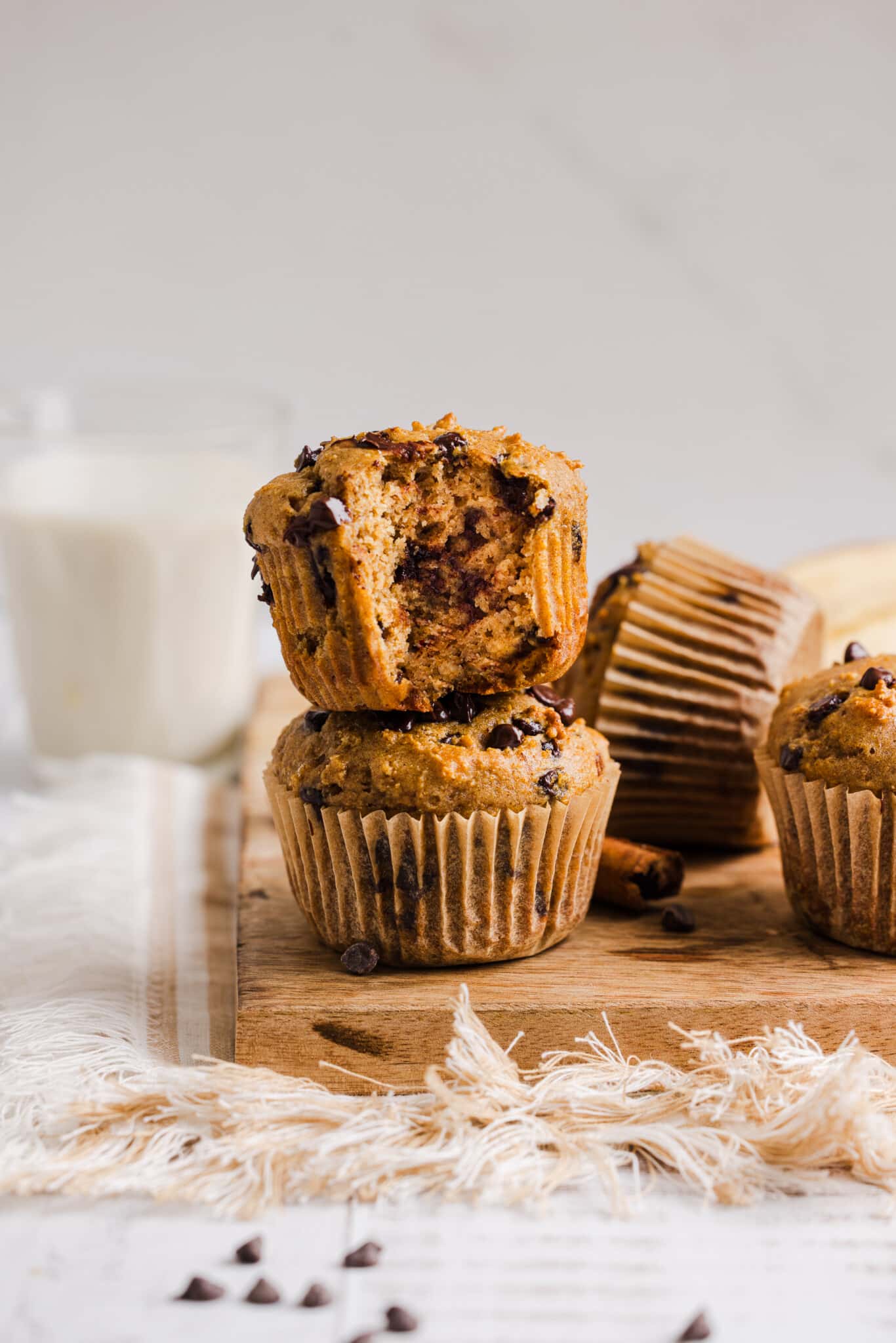 Two banana cottage cheese muffins stacked, one with a bite taken out of it in front of a glass of milk.
