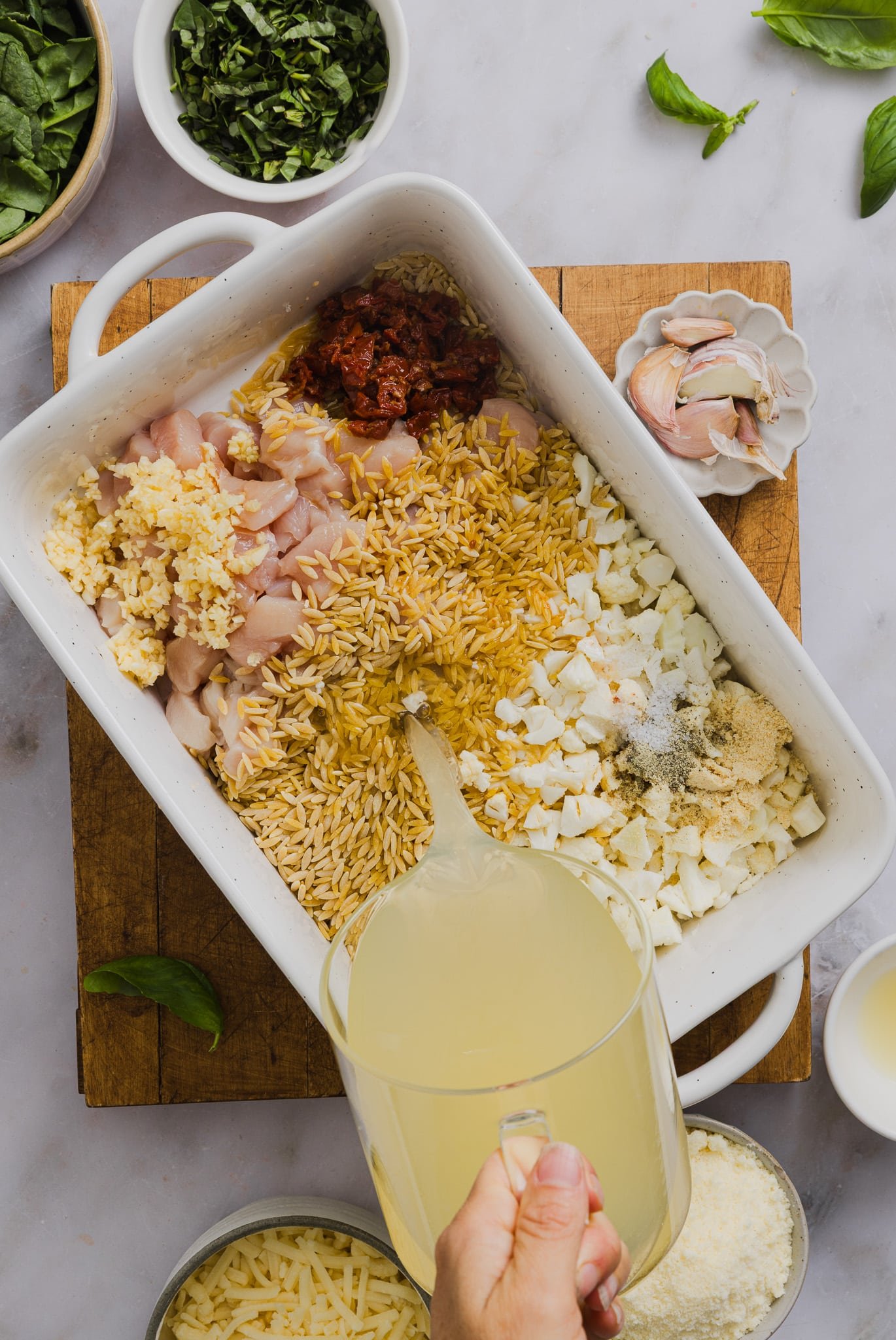 Ingredients for chicken orzo bake being added to a baking dish.