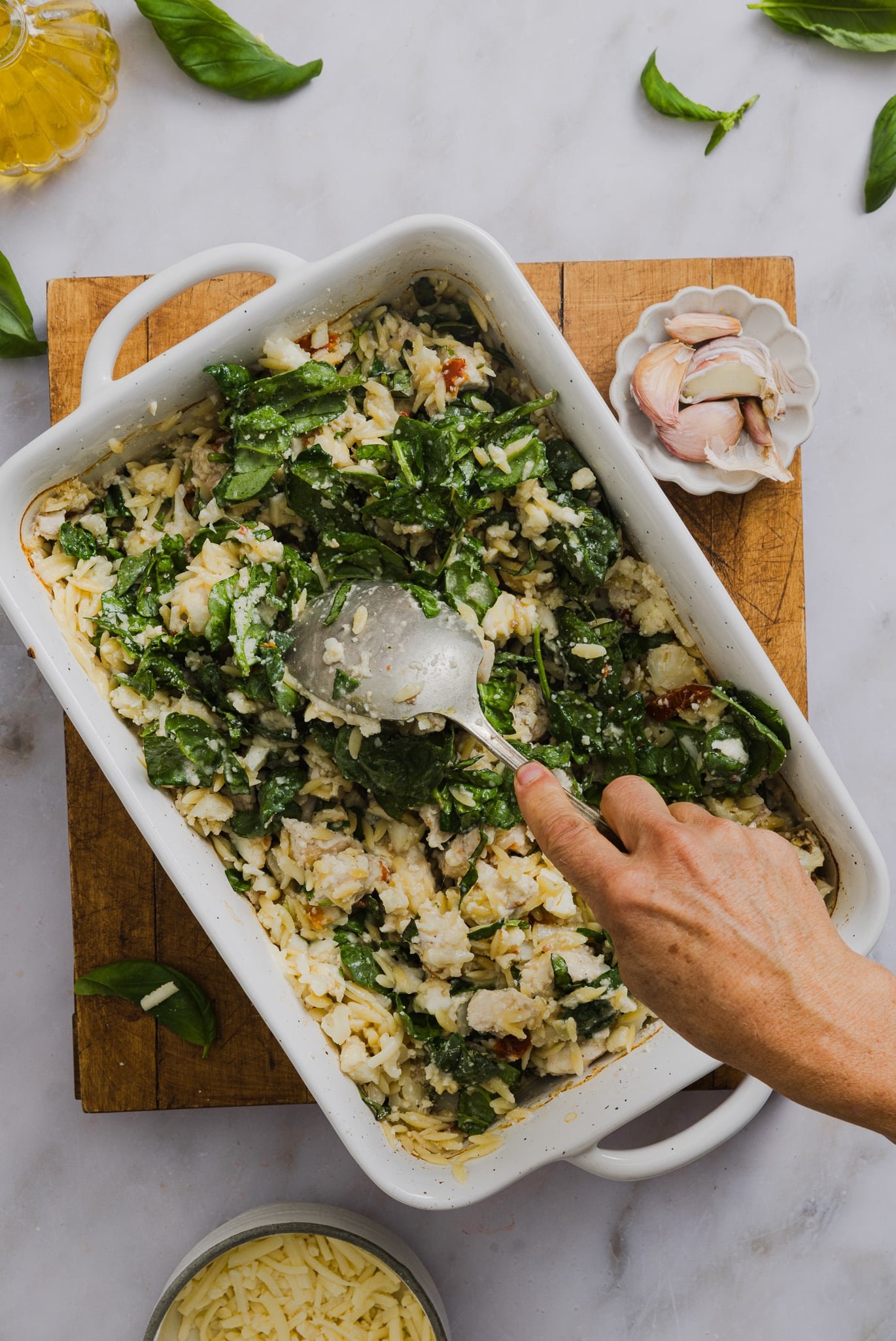 Spinach and cheese being mixed into a chicken orzo bake.