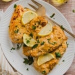 Greek yogurt marinated chicken cooked on a platter garnished with lemon slices, fresh parsley and a large fork.