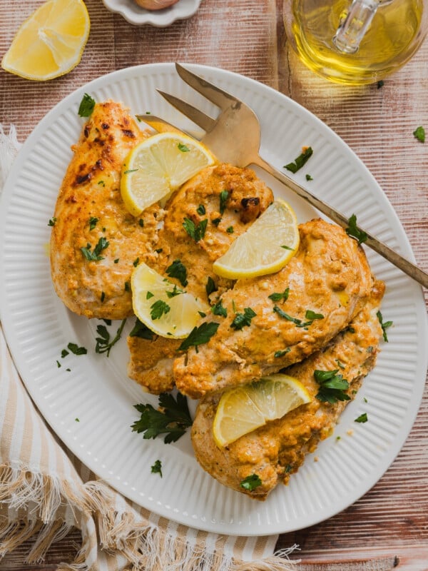 Greek yogurt marinated chicken cooked on a platter garnished with lemon slices, fresh parsley and a large fork.