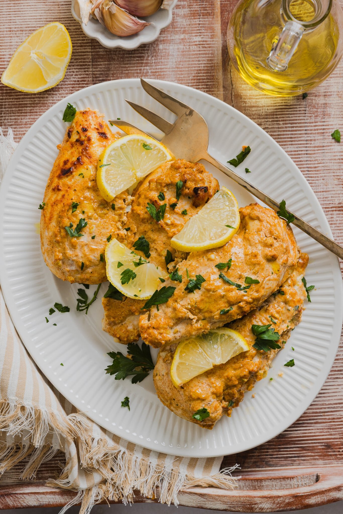 Greek yogurt marinated chicken cooked on a platter garnished with lemon slices, fresh parsley and a large fork.