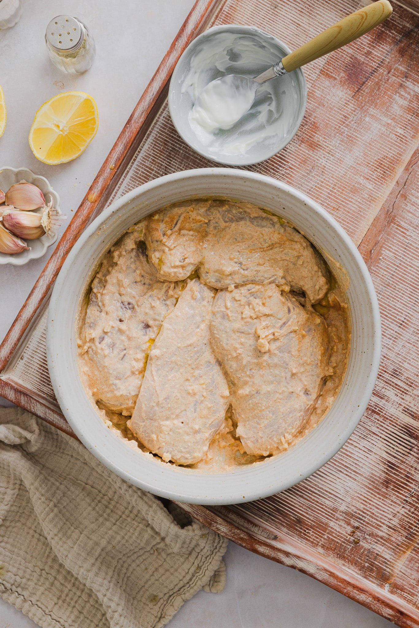 Raw chicken in a bowl coated with Greek yogurt marinade.