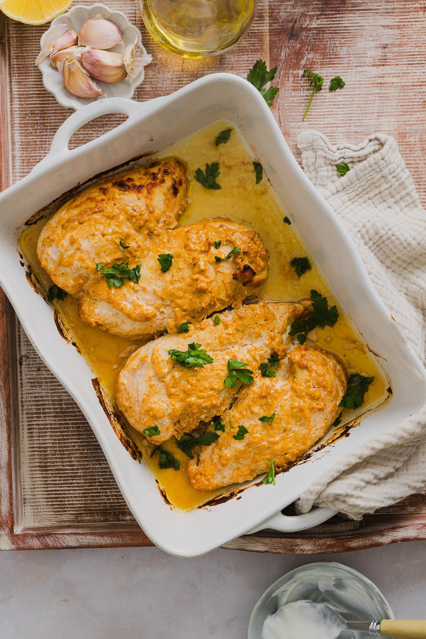Baked Greek yogurt chicken in a large white baking dish garnished with fresh parsley.