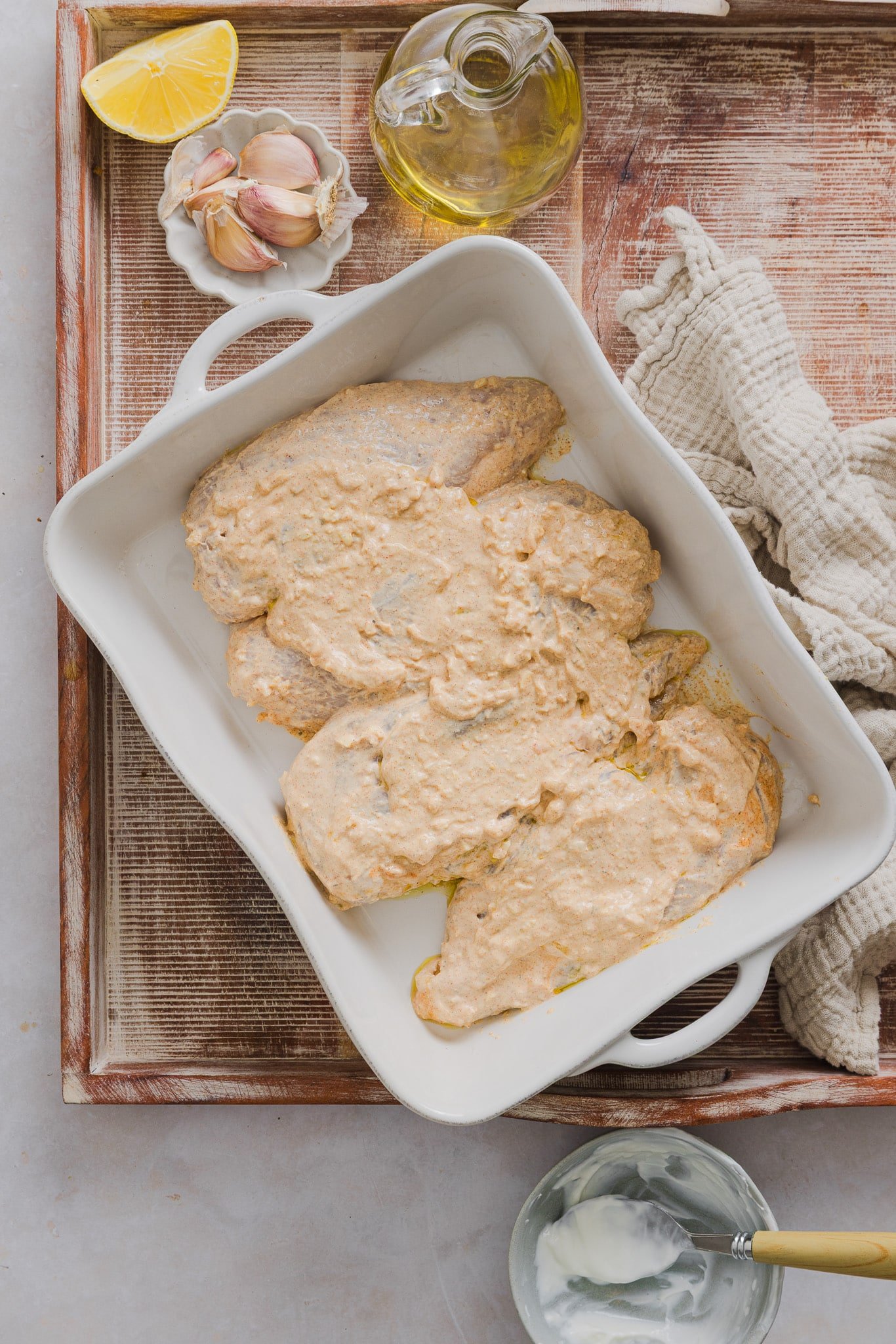 Chicken breast coated in Greek yogurt marinade in a large white baking dish.