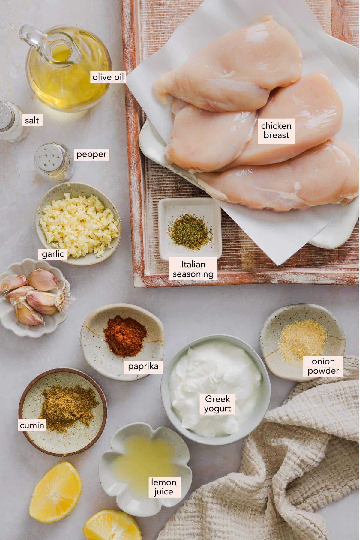 Ingredients for Greek yogurt marinated chicken in individual bowls with labels on a counter top.