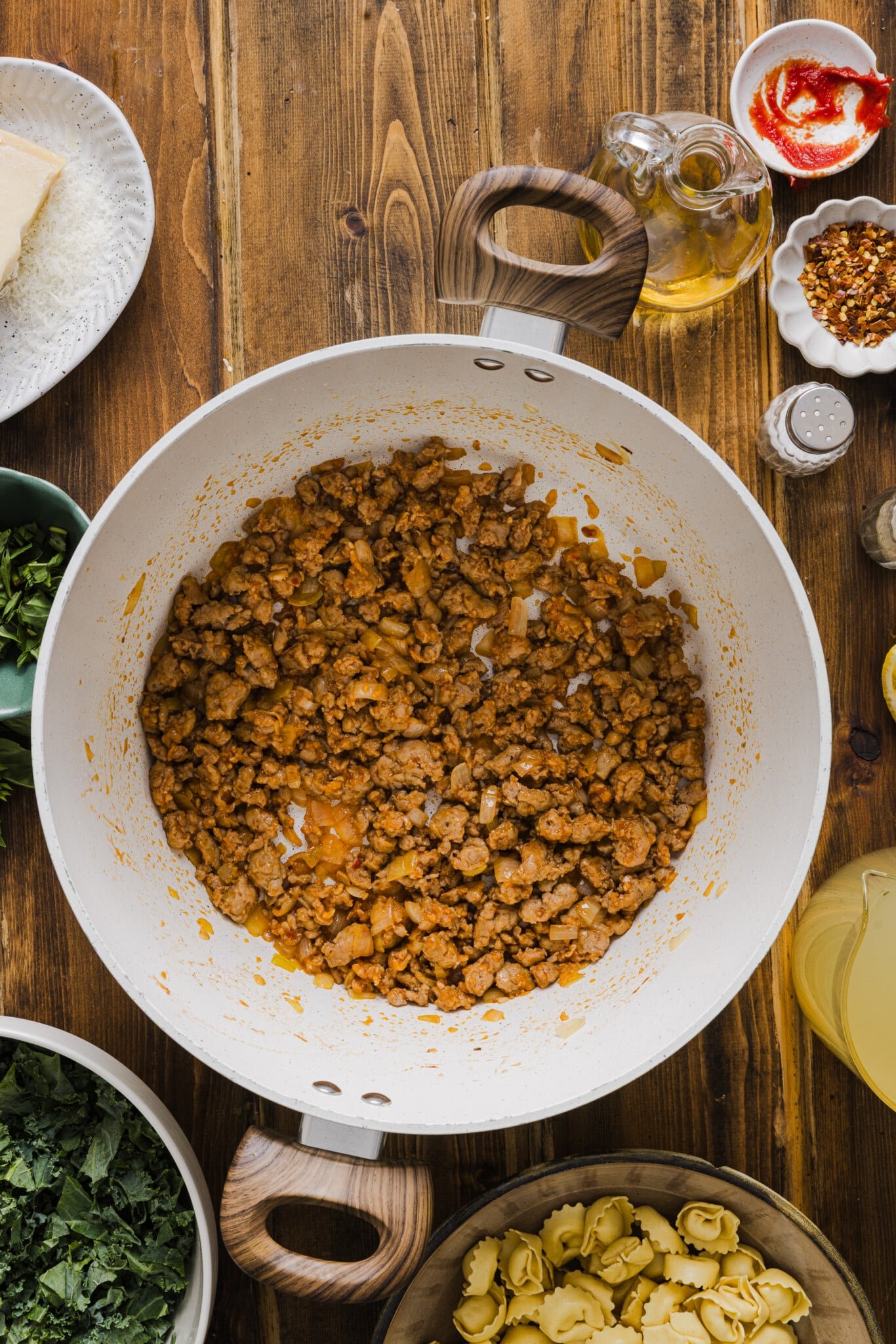 A large soup pot with cooked turkey sausage crumbles, garlic and tomato paste.