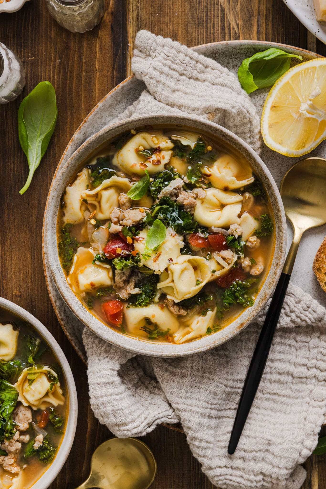 Kale and tortellini soup in a bowl garnished with grated parmesan cheese and red pepper flakes.