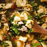 Kale and tortellini soup in a pot with a wooden spoon lifting out a scoop.