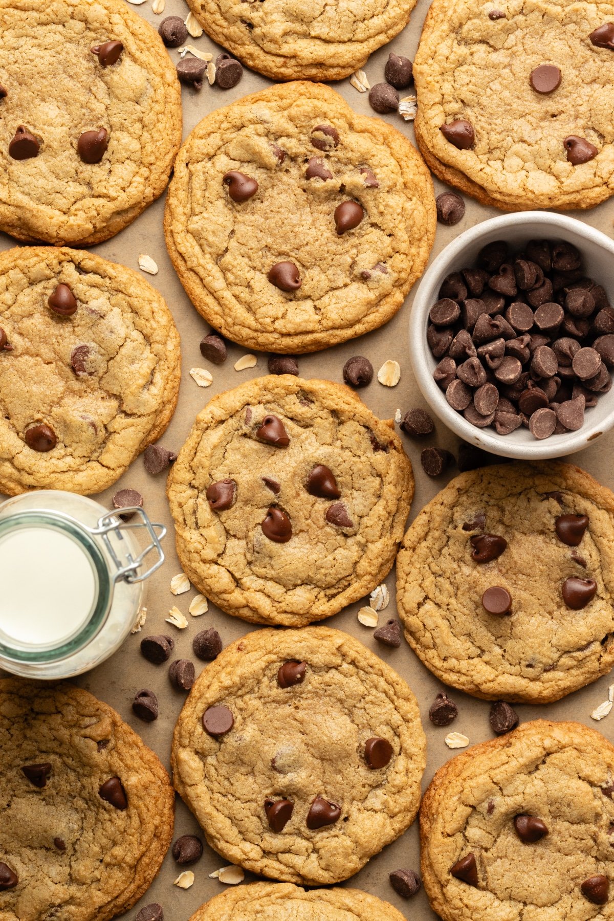 Oat flour chocolate chip cookies on a cookies sheet with a bowl of chocolate chips and a jar of milk.