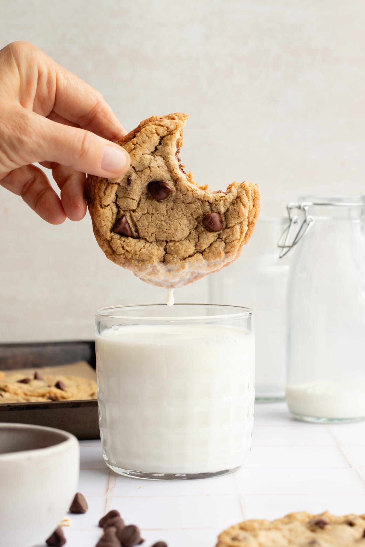 An oat flour cookie with a bite taken out being held over a glass of milk.