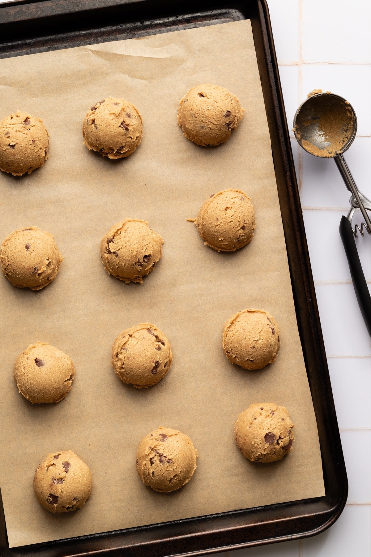 Oat flour cookie dough balls scooped into rows on a parchment lined baking sheet.