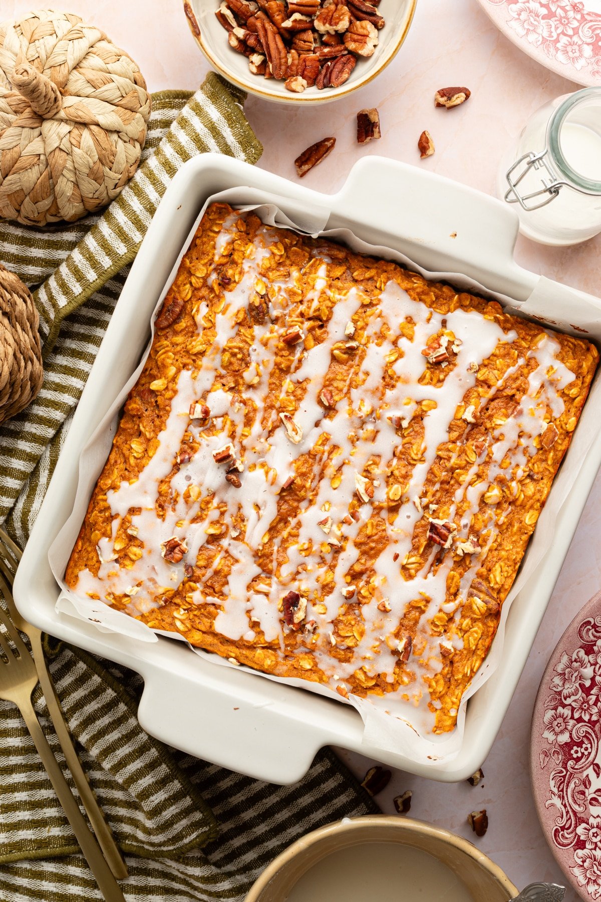 Protein pumpkin baked oats in a square white pan with a drizzle of powdered sugar glaze.