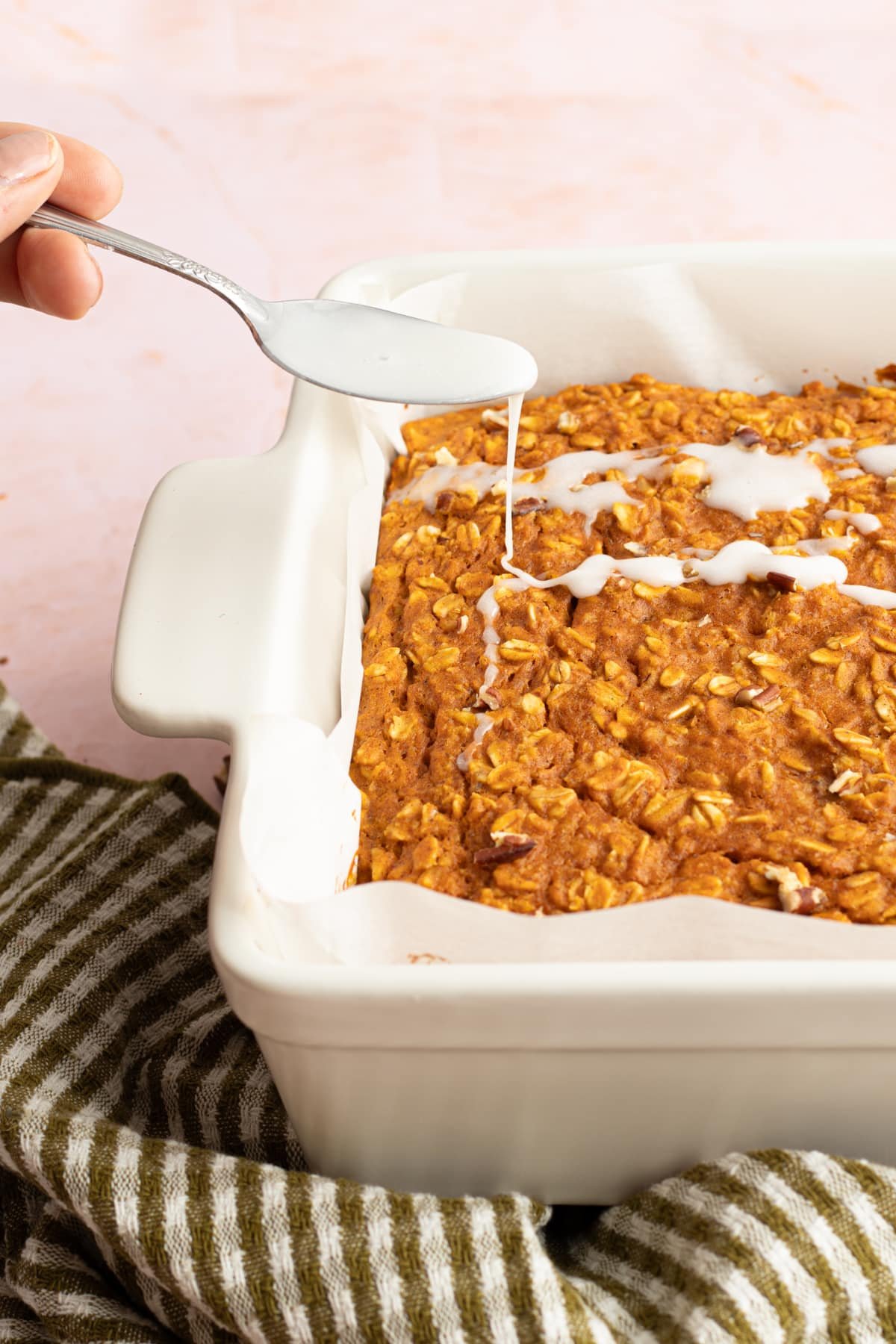 Baked protein pumpkin baked oats being drizzled with glaze from a spoon.