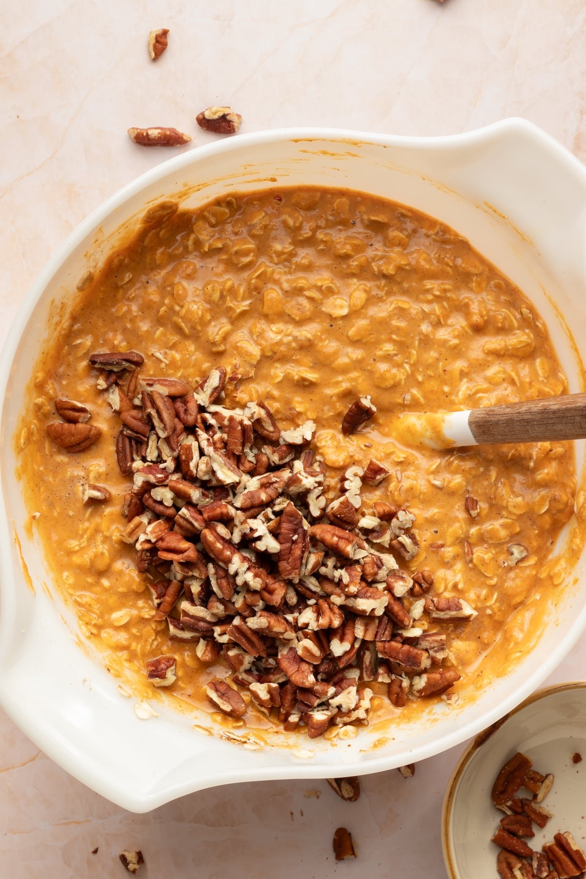 Chopped pecans being folded into protein pumpkin baked oat batter.