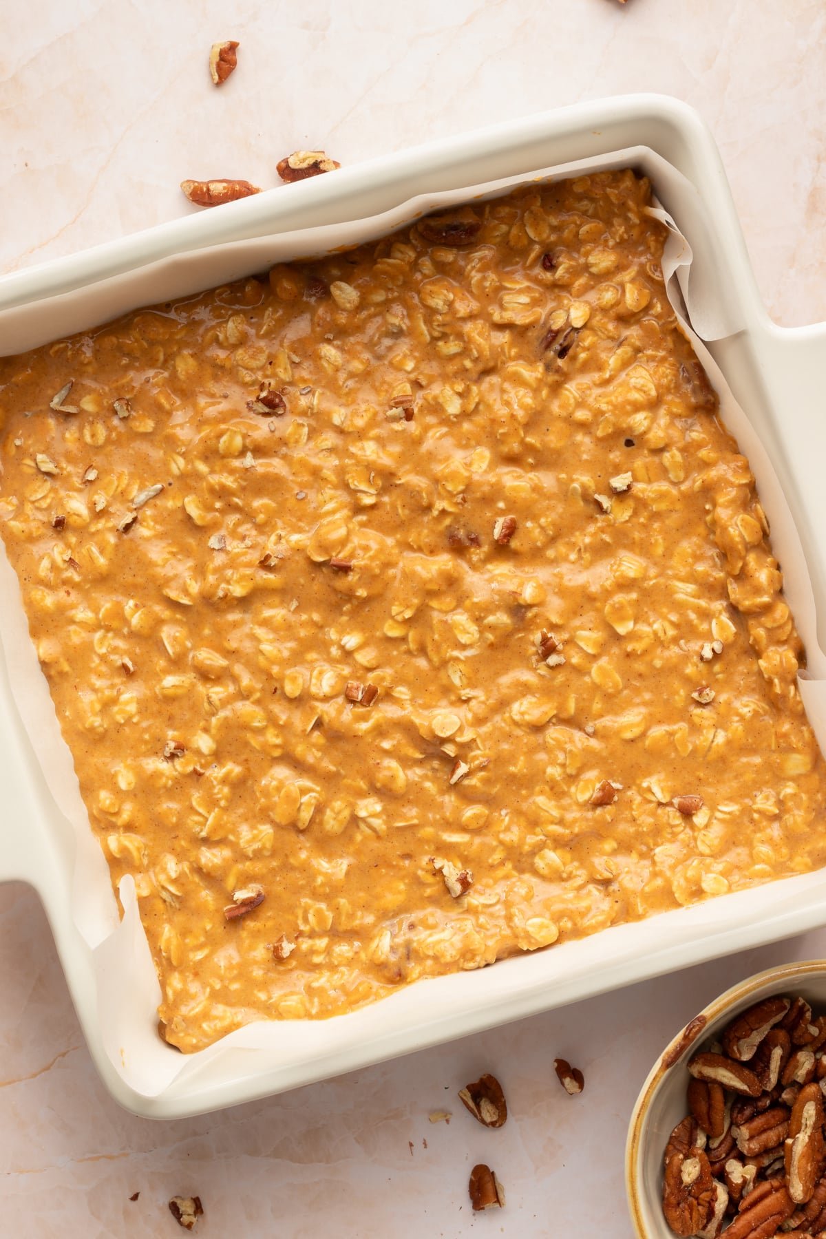 Protein pumpkin baked oat mixture in a parchment lined square baking dish ready for the oven.