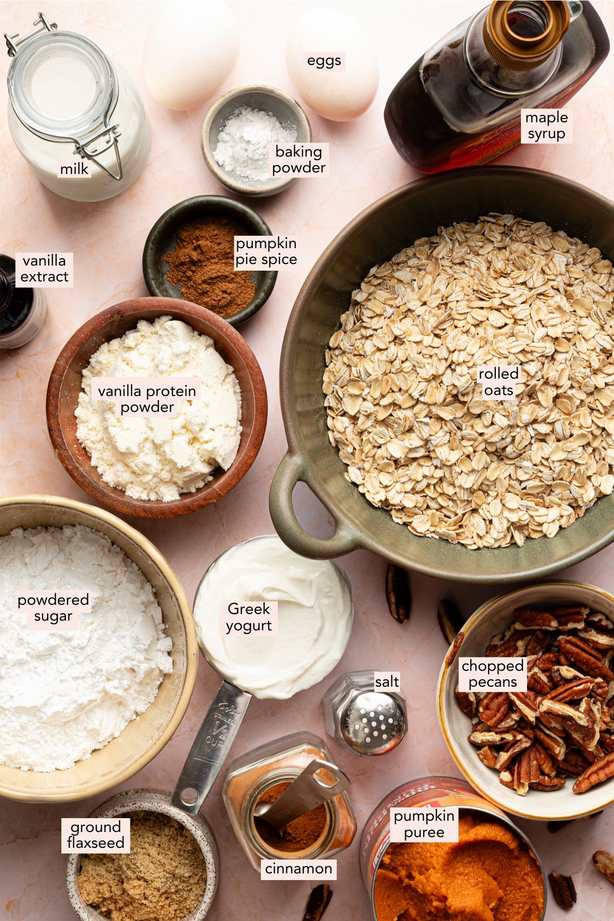 Ingredients for protein pumpkin baked oats in individual bowls on a pink countertop.